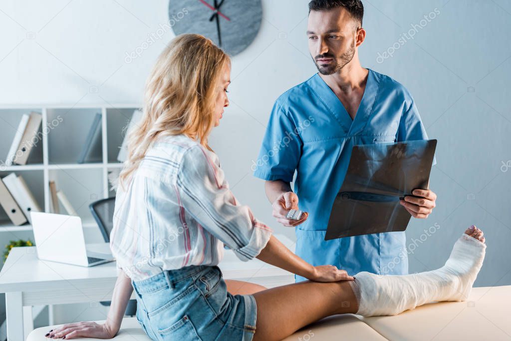 bearded orthopedist holding x-ray and giving pills to injured woman 