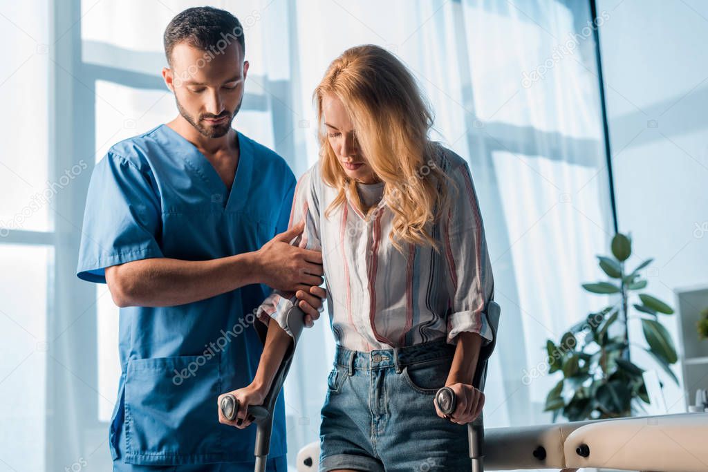 handsome doctor standing near woman with crutches 