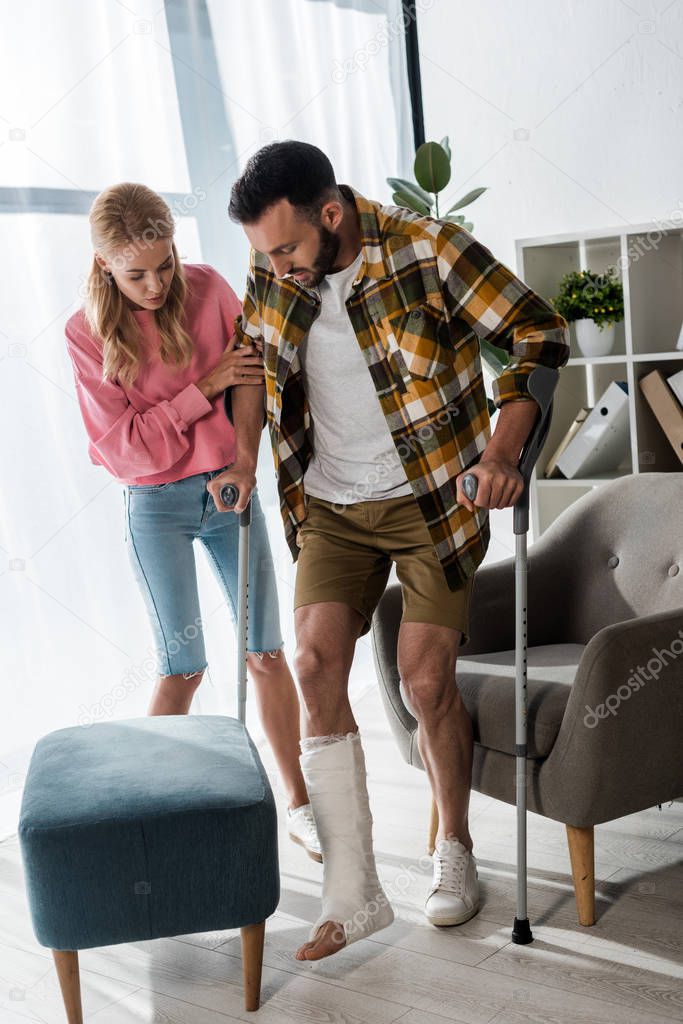 attractive woman helping injured man with crutches at home 