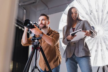 low angle view of photographer taking photo and producer looking at paper on backstage  clipart