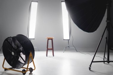 digital camera, fan, reflector, wooden stool and lights on backstage in photo studio clipart
