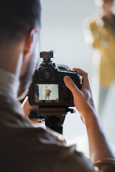 selective focus of photographer taking photo of model with digital camera on backstage