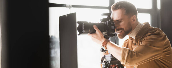 panoramic shot of smiling photographer taking photo with digital camera on backstage