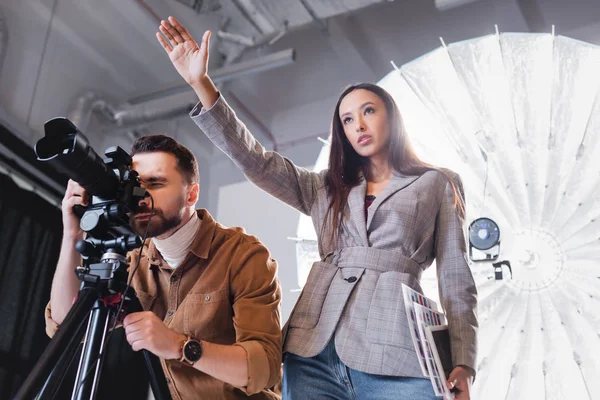 Niski Kąt Widzenia Fotografa Robiącego Zdjęcia Producenta Wskazującego Ręką Kulisami — Zdjęcie stockowe