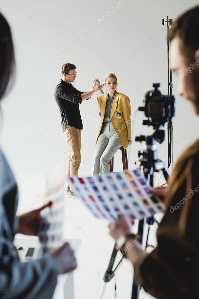 selective focus of hairstylist doing hairstyle to stylish model and producer with photographer on backstage 