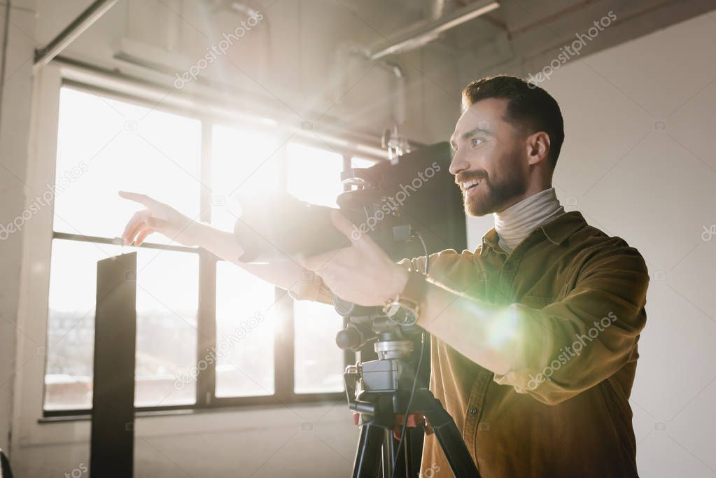 smiling photographer taking photo with digital camera and pointing with finger on backstage