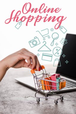 Beyaz, e-ticaret konsepti üzerine çevrimiçi alışveriş mektuplarının yanında oyuncak alışveriş arabası taşıyan bir kadının görüntüsü.