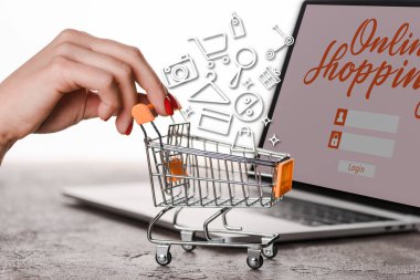 Beyaz, e-ticaret konsepti üzerine resimli dizüstü bilgisayarın yanında oyuncak alışveriş arabası tutan bir kadın görüntüsü.
