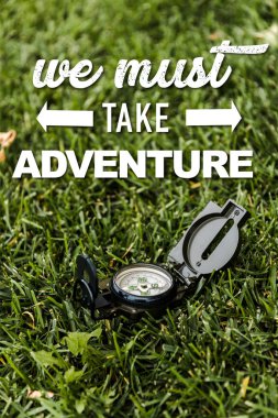 selective focus of black vintage compass on green grass near we must take adventure letters  clipart