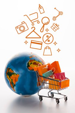 Dünya yakınındaki alışveriş torbalarıyla oyuncak alışveriş arabasının seçici odak noktası ve beyaz, e-ticaret konsepti