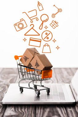 selective focus of toy shopping cart with small carton boxes on laptop keyboard near illustration on white, e-commerce concept clipart
