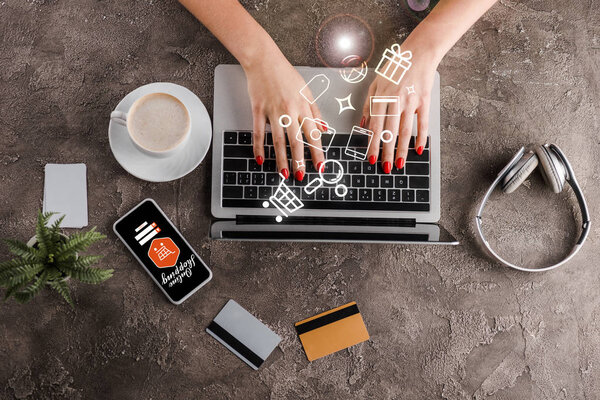 top view of woman using laptop near smartphone, cup of coffee, plant, headphones credit cards and illustration, e-commerce concept