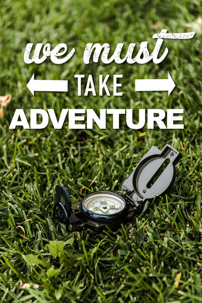 selective focus of black vintage compass on green grass near we must take adventure letters 