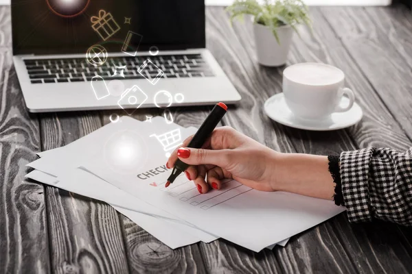 チェックリスト イラスト テーブルの上のカップとラップトップ 電子商取引の概念の近くに赤いマーカーペンを保持している実業家のクロップドビュー — ストック写真