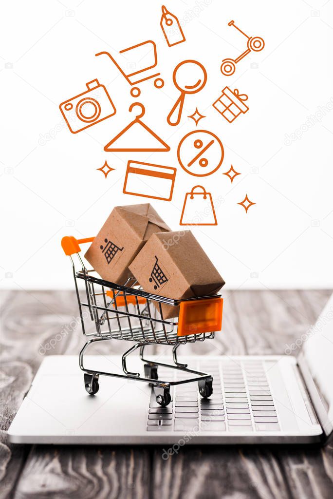 selective focus of toy shopping cart with small carton boxes on laptop keyboard near illustration on white, e-commerce concept