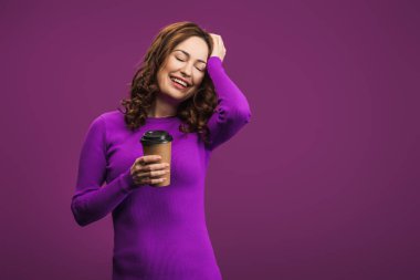 laughing girl touching head while holding coffee to go on purple background clipart