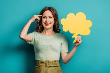 cheerful woman showing idea sign while holding thought bubble on blue background clipart