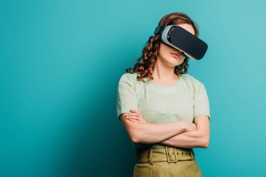Mavi arka planda çapraz kolları olan VR kulaklıklı şüpheli kız.