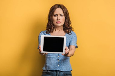 sarı arkaplanda boş ekranlı dijital tablet gösteren rahatsız kadın