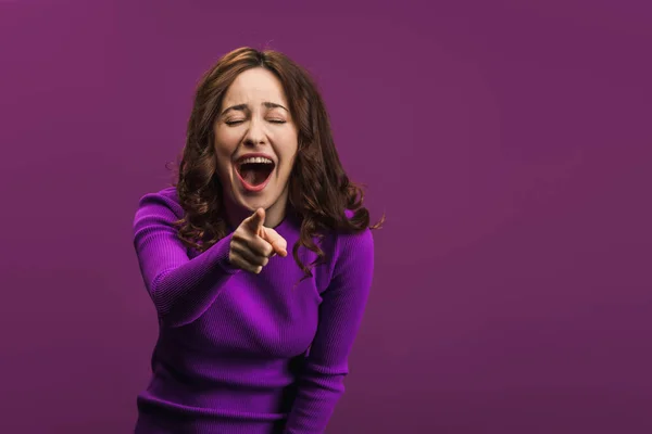 Весела Жінка Сміється Закритими Очима Вказує Пальцем Камеру Фіолетовому Фоні — стокове фото