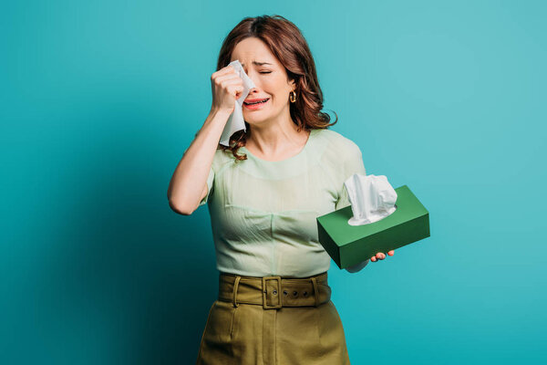 crying woman wiping tears with paper napkins on blue background