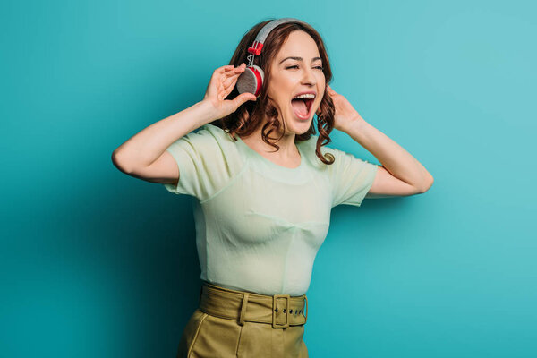 excited girl singing in wireless headphones on blue background