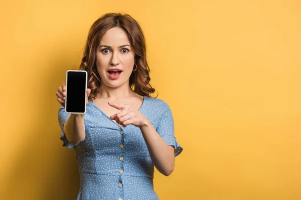 Surprised Woman Pointing Finger Smartphone Blank Screen Yellow Background — Stock Photo, Image