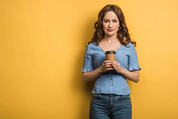 Uśmiechnięta Młoda Kobieta Trzymająca Kawę Wynos Patrząc Kamerę Żółtym Tle — Zdjęcie stockowe
