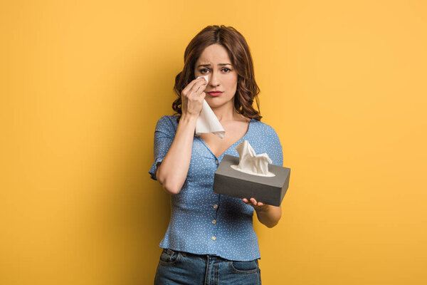 upset girl covering tears with paper napkin on yellow background