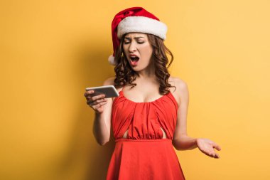 Sarı arka planda video görüşmesinde bağıran Noel Baba şapkalı kızgın kız.