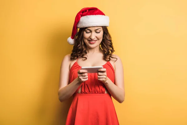 Cheerful Girl Santa Hat Messaging Smartphone Yellow Background — 스톡 사진