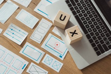 Bilgisayarında ux harfli küplerin yüksek açılı görünümü ve ahşap masadaki web sitesi çizimleri.