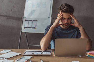 Çalışma masasında dizüstü bilgisayarı ve düzeni olan konsantre tasarımcının seçici odak noktası
