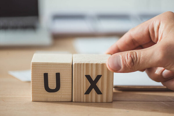 Обрезанный вид человека, держащего деревянный куб с буквами ux за деревянным столом
