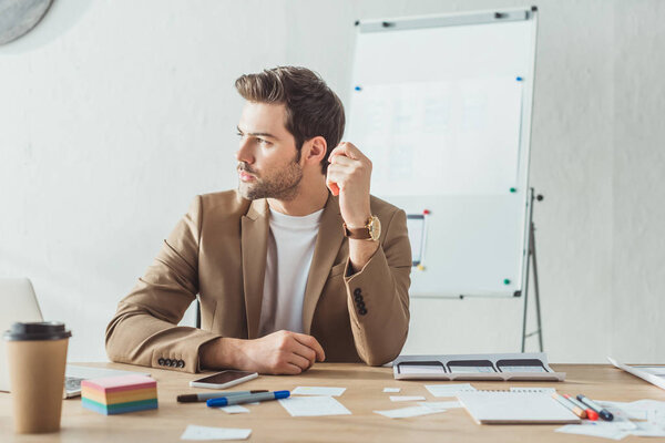 Креативный дизайнер смотрит в сторону стола с макетами мобильных приложений на столе

