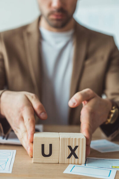 Cropped view of designer holding cubes with ux letters at table with sketches