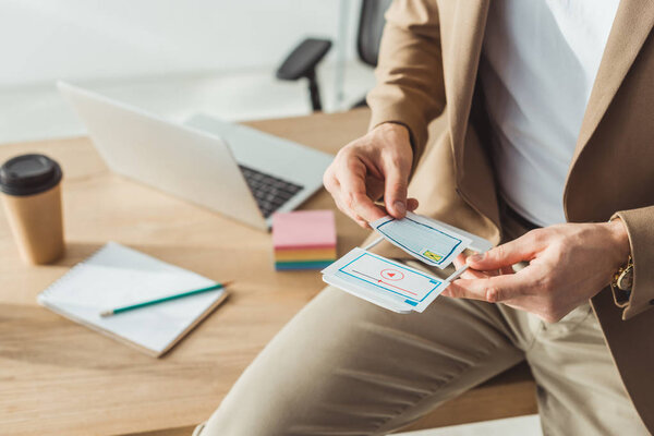Cropped view of designer planning mobile website design with layouts by table
