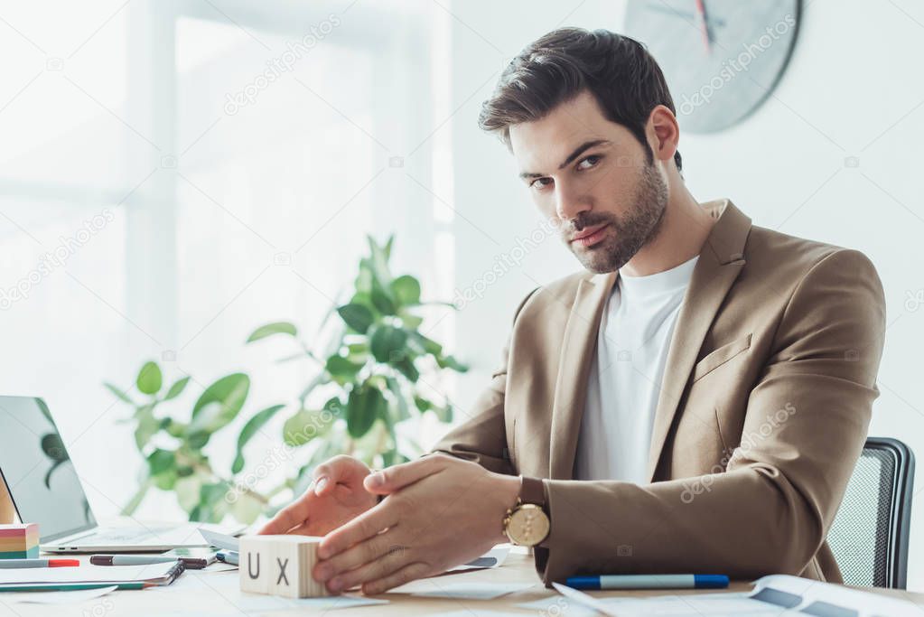 Handsome designer looking at camera while holding cubes with ux letters at working table