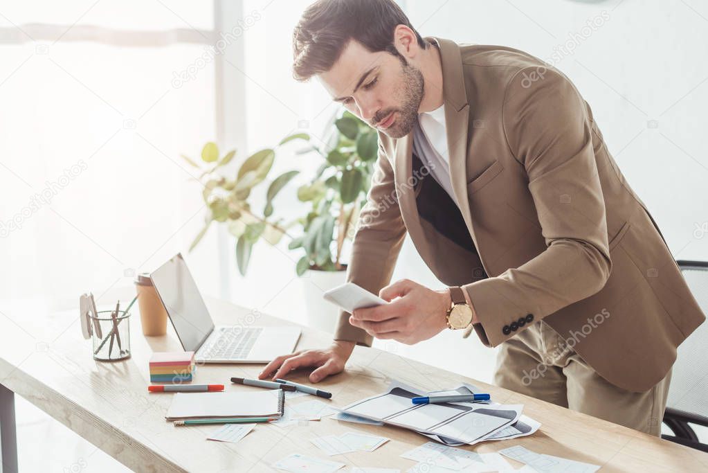 Side view of handsome designer using smartphone while developing user experience design in office