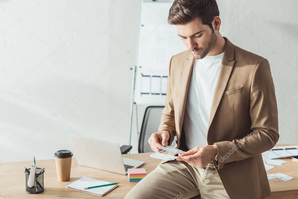 Handsome designer developing mobile website design with layouts by office table
