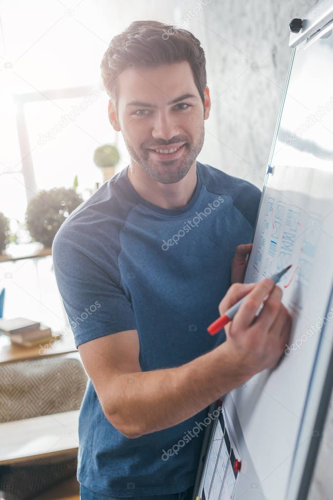 Handsome ux developer smiling at camera while sketching website template on whiteboard in office