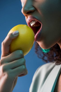 Mavi üzerine izole edilmiş limon yiyen diş telli Afrikalı Amerikalı kadın manzarası.