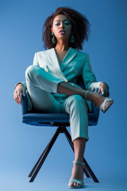 Afro-Amerikan kadın mavi arka planda koltukta oturuyor. 