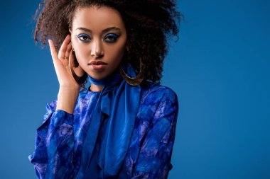 Çekici Afro-Amerikan kadın. Elbise ve küpeler içinde. Mavi renkli kameraya bakıyor. 