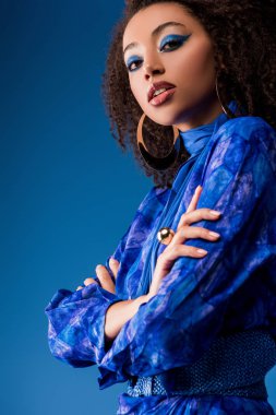 Çekici Afro-Amerikan kadınının düşük açılı görüntüsü şık giyinmiş mavi renkli kameraya bakıyor. 