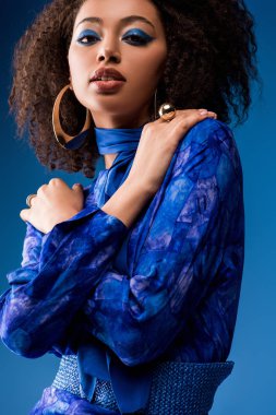 Makyajlı şık Afro-Amerikan kadın mavi kameraya bakıyor. 