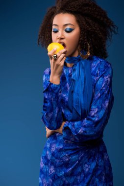 Afro-Amerikalı bir kadın mavi üzerine izole edilmiş lezzetli limon yiyor.