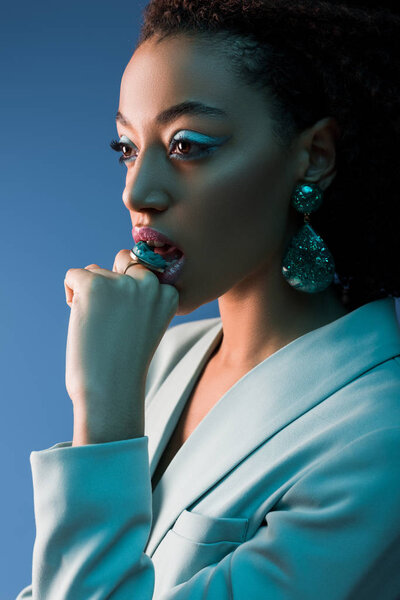 attractive and stylish african american woman biting ring isolated on blue