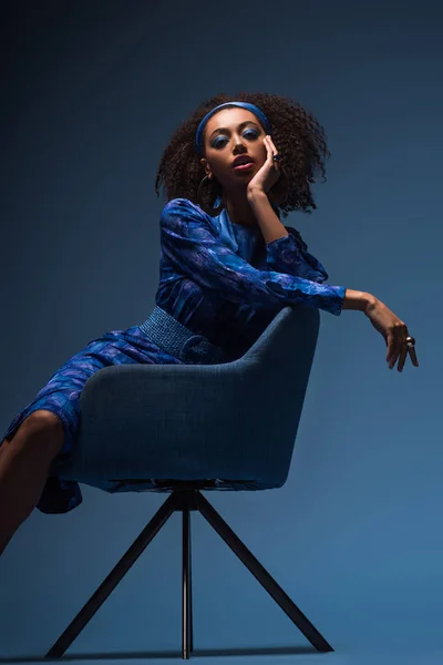 Ελκυστική Αφροαμερικανή Γυναίκα Κάθεται Στην Πολυθρόνα Μπλε Φόντο — Φωτογραφία Αρχείου