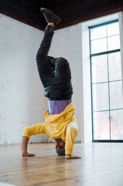 man in hat breakdancing and doing handstand in dance studio  clipart
